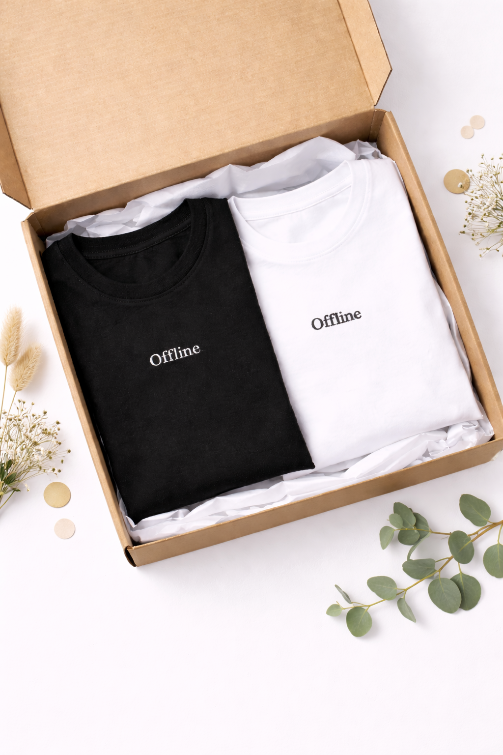 Two t-shirts, one black and one white, with 'Offline' text in a cardboard box on a light surface.