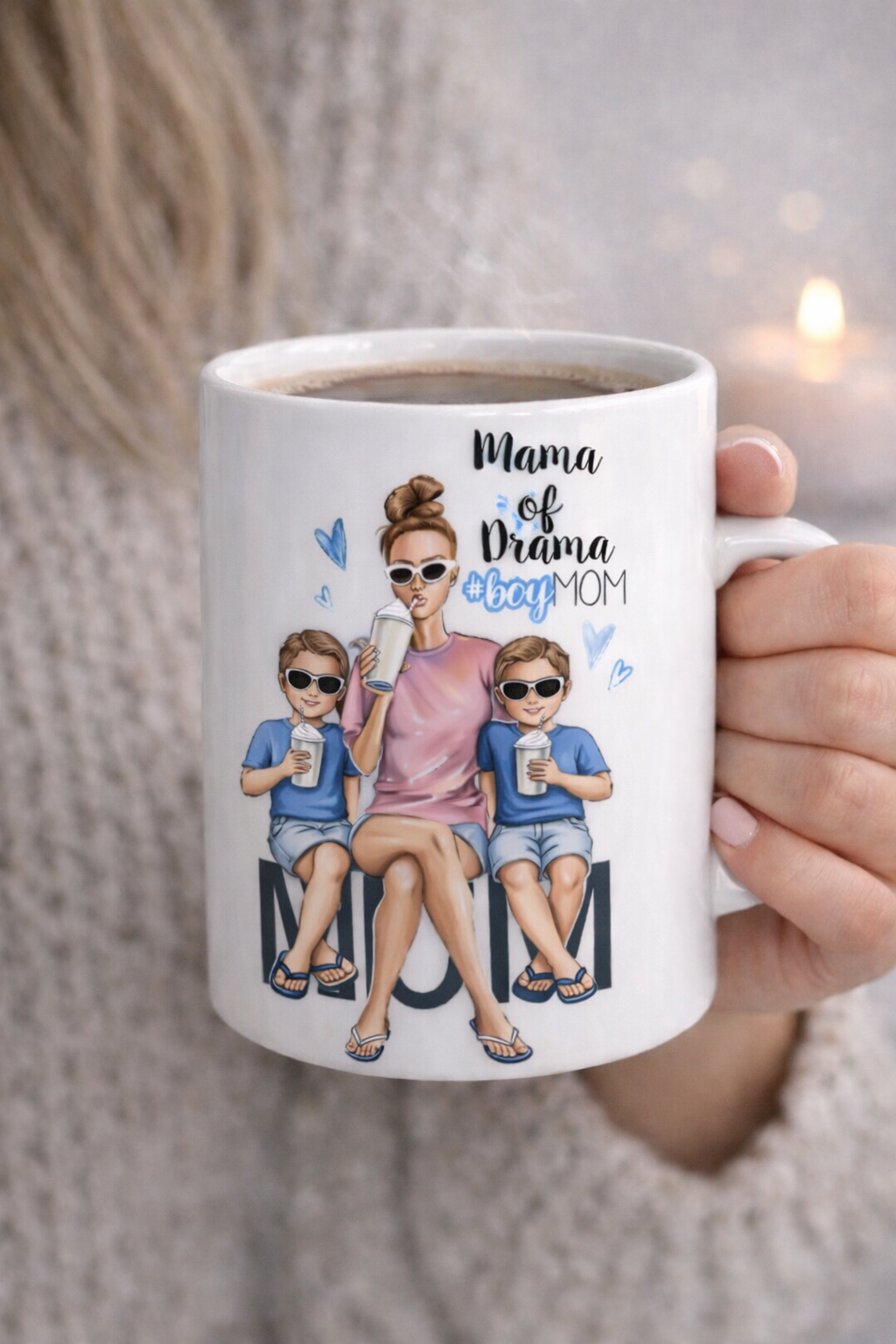 White ceramic coffee mug with illustrated mom and two boys wearing sunglasses and holding drinks, featuring the text “Mama of Drama #boyMOM”.