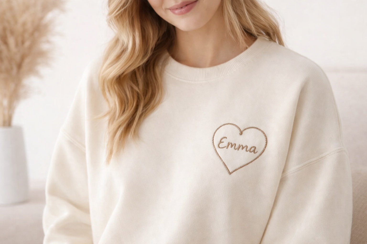 Woman wearing a cream sweatshirt with a personalized heart embroidery and custom name on the left chest

