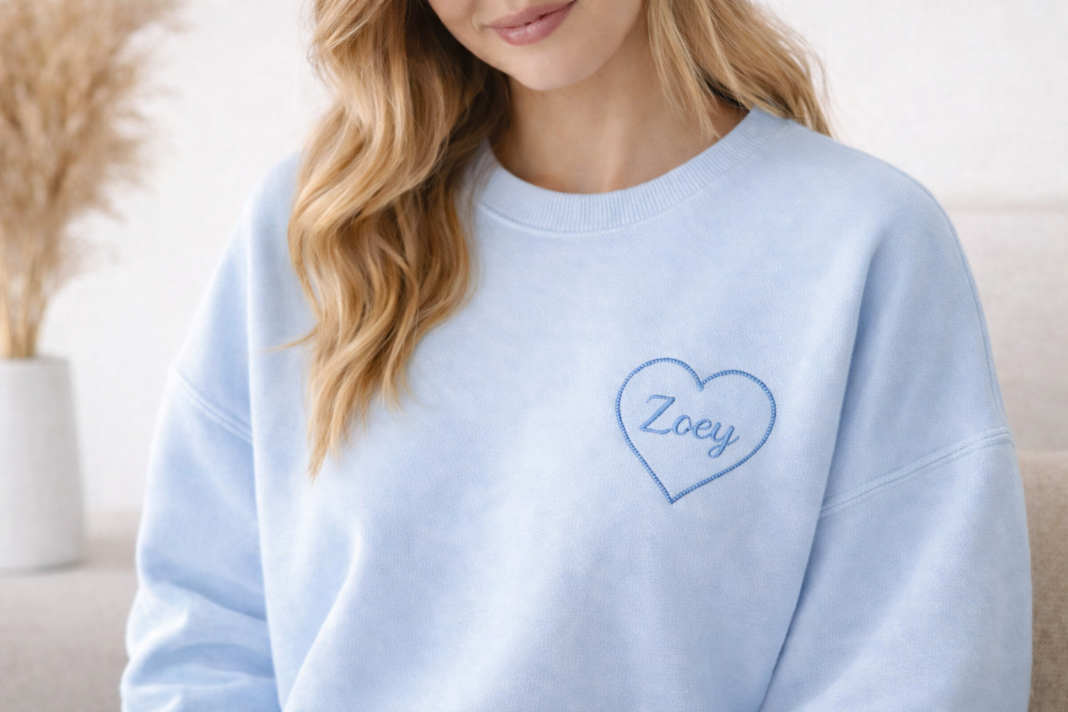 Light blue personalized sweatshirt with heart embroidery and the name Zoey worn by a woman
